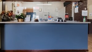 Una recepción con un cartel de registro, un terminal de pagos con Visa, un teléfono y un anuncio de servicio de lavandería las 24 horas.