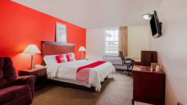 Habitación de hotel con cama, escritorio, silla, televisor y ventana con cortinas.