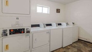 Un cuarto de lavandería con cuatro lavadoras y secadoras apiladas, una ventana y una pequeña imagen en la pared.