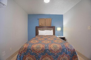 Un dormitorio con una colcha estampada, un cabecero de madera, una mesita de noche con lámpara y una ventana con cortinas.
