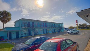 A building with a blue exterior, a staircase, and a parking lot with cars. - Queen Bed|Kitchenette|Non-Smoking (Merritt Island FL)