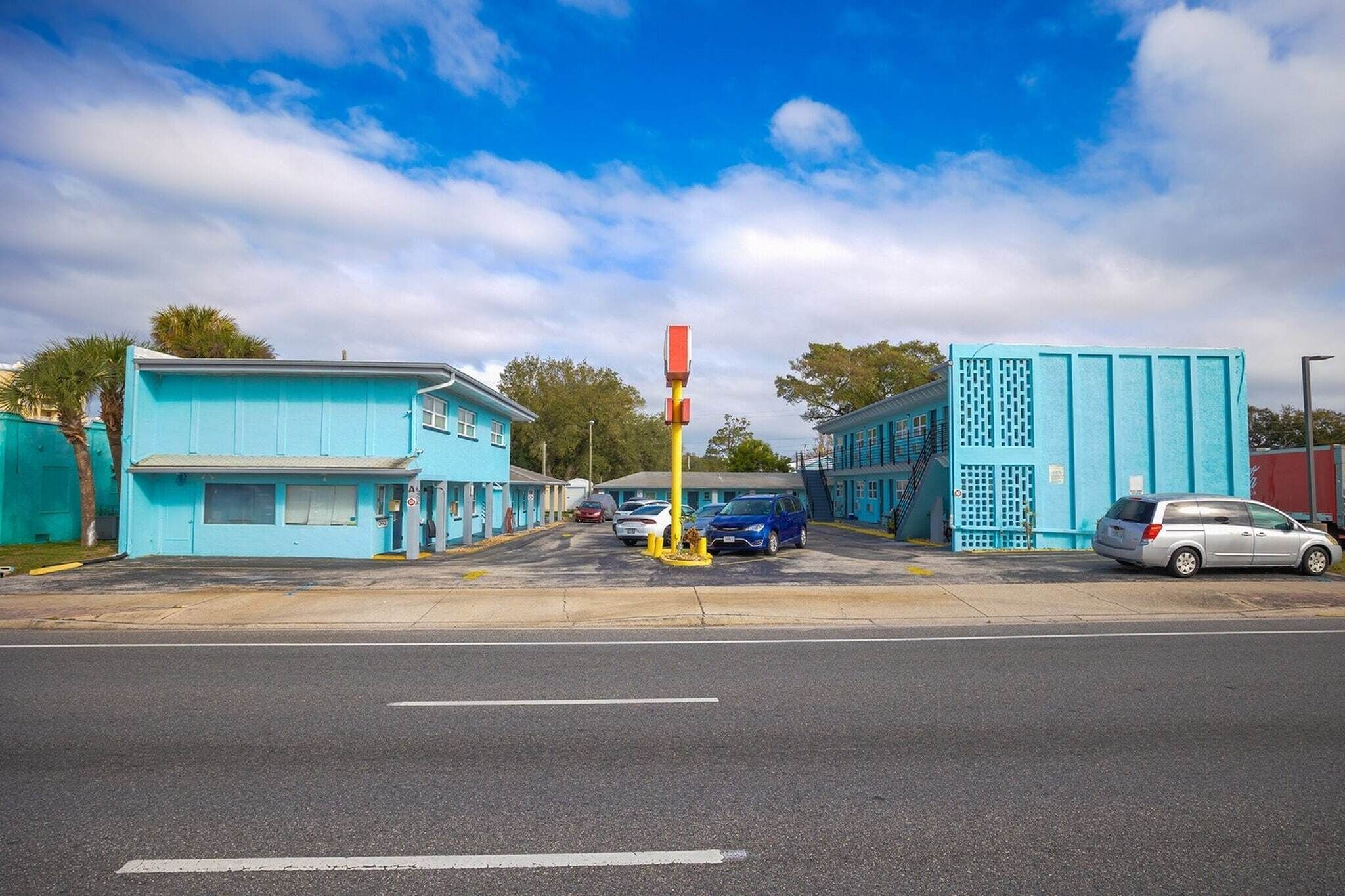 A street view with blue buildings, a yellow pole, and parked cars.