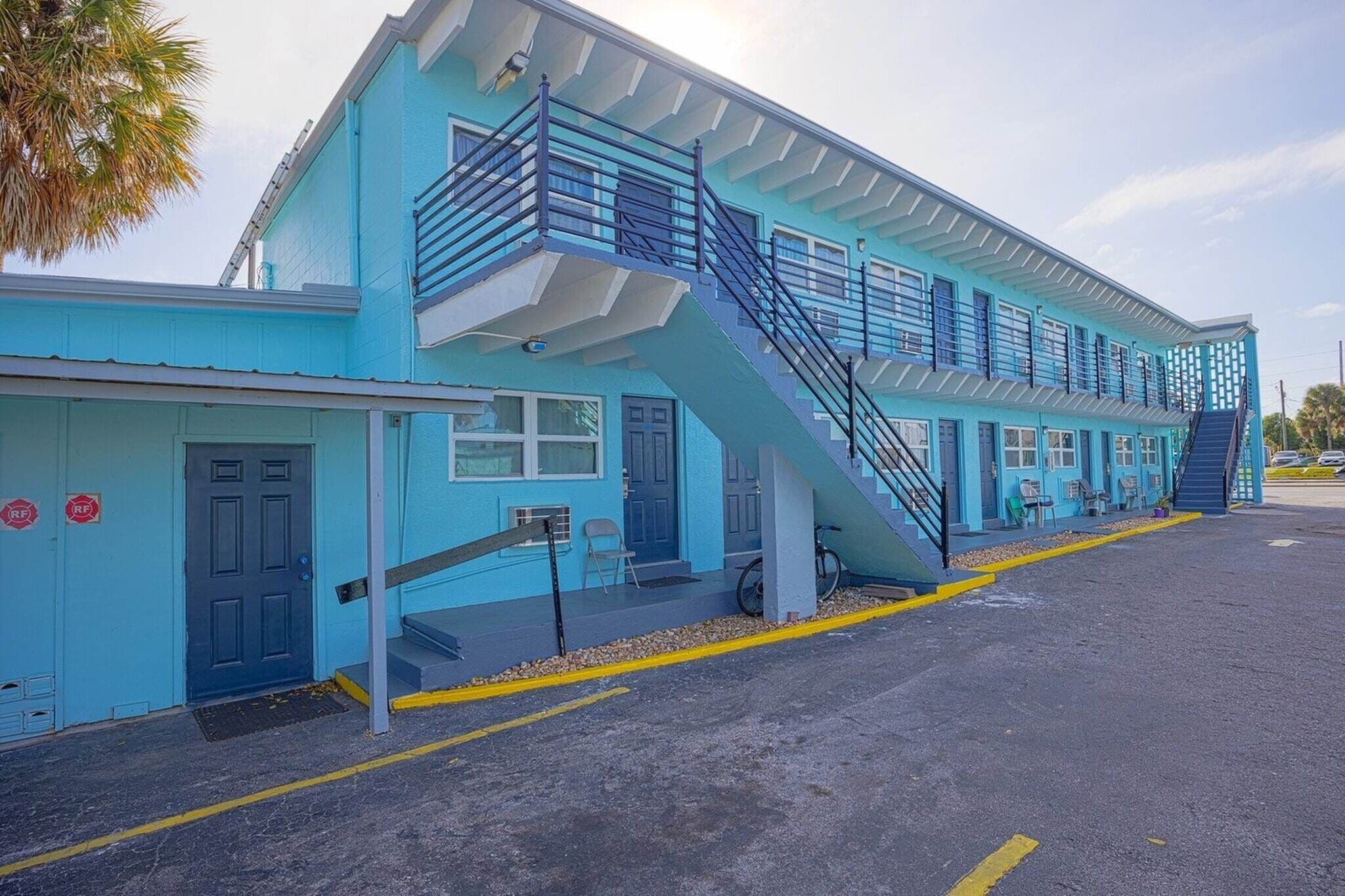 Um edifício azul com escadas, porta e estacionamento.