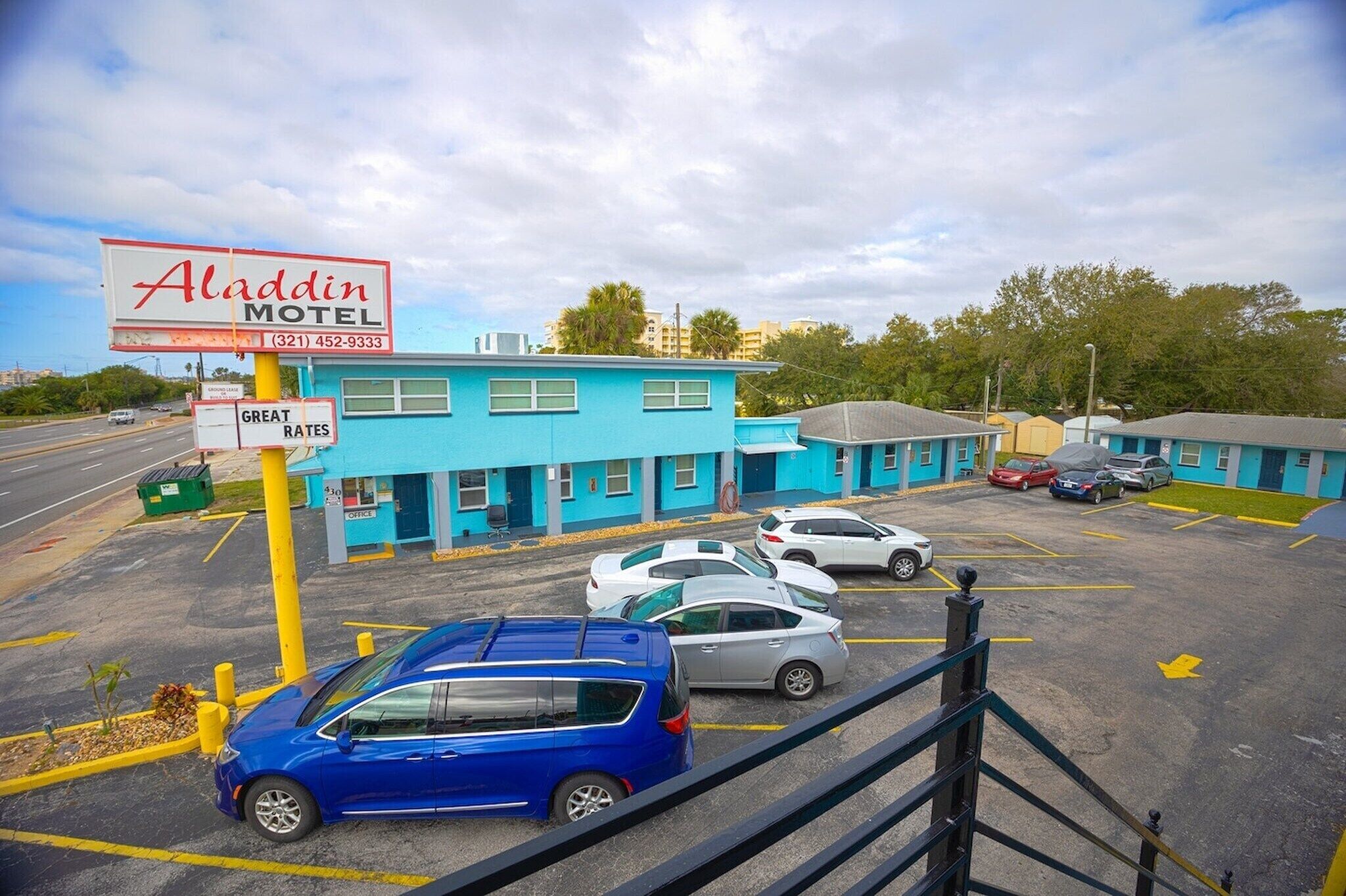 Een motel met een blauwe gevel, een bord en een parkeerplaats met meerdere auto's.