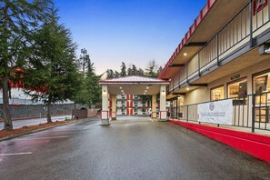 A hotel entrance with a covered parking area, a red and beige building facade, and a banner indicating the hotel's name. - Queen Bed Accessible|Nsmk (Renton WA)