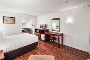 A hotel room with a bed, a desk, a chair, a television, and a mirror.