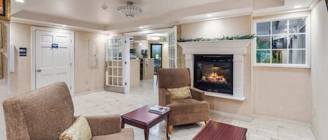 A living room with a fireplace, two armchairs, a coffee table, and a door leading to a kitchen.