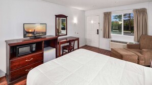 A hotel room with a bed, a desk with a computer, a television, a chair, and a window with curtains. - Queen Bed |Renton WA (Renton WA)