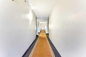 A long, narrow hallway with a patterned carpet and white walls. - King Bed Accessible|Nsmk (Oklahoma City OK)