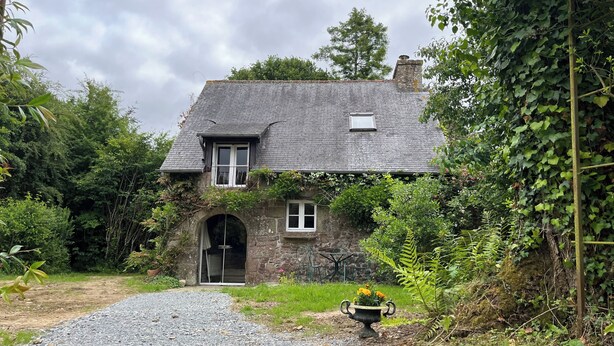 Una casa de piedra con un camino de grava que conduce a la entrada, rodeada de vegetación.