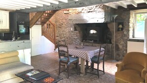 Un interior rústico con chimenea de piedra, una mesa de comedor con sillas, un sofá y una zona de cocina con electrodomésticos.