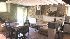 Un interior rústico con una pared de piedra, una mesa de comedor con sillas, un sofá y una zona de cocina con fregadero y estufa.