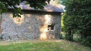 Un edificio de piedra con una ventana y una puerta pequeña, rodeado de hierba y árboles.