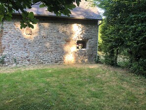 A stone building with a window and a small door, surrounded by grass and trees.