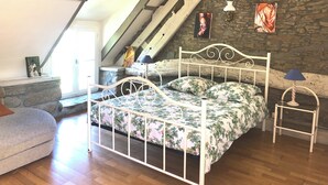 Un dormitorio con techo inclinado, pared de piedra, cama con ropa de cama floral, una mesita y una lámpara.