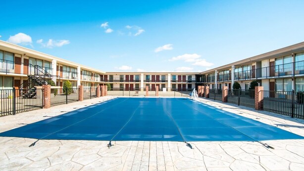 Un hotel con piscina centrale, pilastri in mattoni e cielo azzurro.
