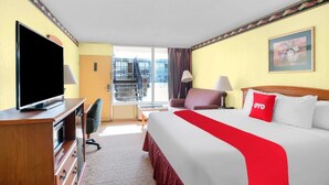 Una camera d'albergo con un letto, televisione, una scrivania, una sedia, una finestra vista e un balcone.