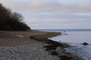 Ein kiesiger Strand mit felsigem Ufer und spärlicher Vegetation.
