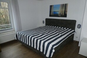 Ein Schlafzimmer mit Bett, Fenster, einem Bild an der Wand und einer Heizung.