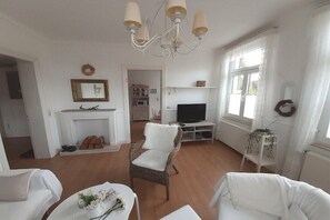 Ein Wohnzimmer mit Kamin, Fernseher, Korbsesseln und einer Kandelaber.