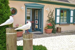 Ein Gebäude mit einer blauen Tür, hölzernen Pfosten mit Vogel-Skulpturen und Blumentöpfen.