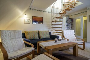 Ein Wohnzimmer mit einer Couch, zwei Sesseln, einem Couchtisch, einer Wendeltreppe und einem Bücherregal.