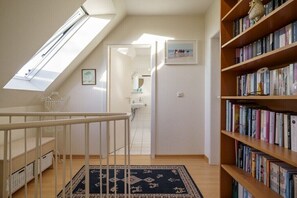 Ein Zimmer mit Oberlicht, einem Bücherregal, einem gemusterten Teppich und einer Tür zu einem anderen Raum.