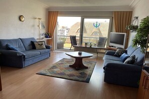 A living room with two sofas, a coffee table, a TV, and a balcony with a view of buildings. - Silver Beach 5 - Coastal Magic (De Haan)
