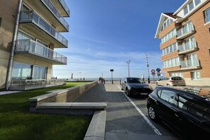 A coastal building with balconies, a paved walkway, and parked cars. - Silver Beach 5 - Coastal Magic (De Haan)