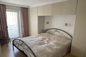 A bedroom with a bed, a chair, a window with curtains, and a balcony. - Silver Beach 5 - Coastal Magic (De Haan)