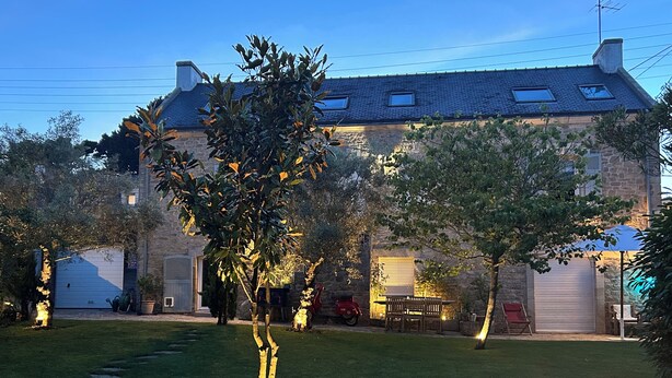 Ein Steinhaus mit geneigtem Dach, einer Garage und einem gepflegten Rasen mit einem Baum.