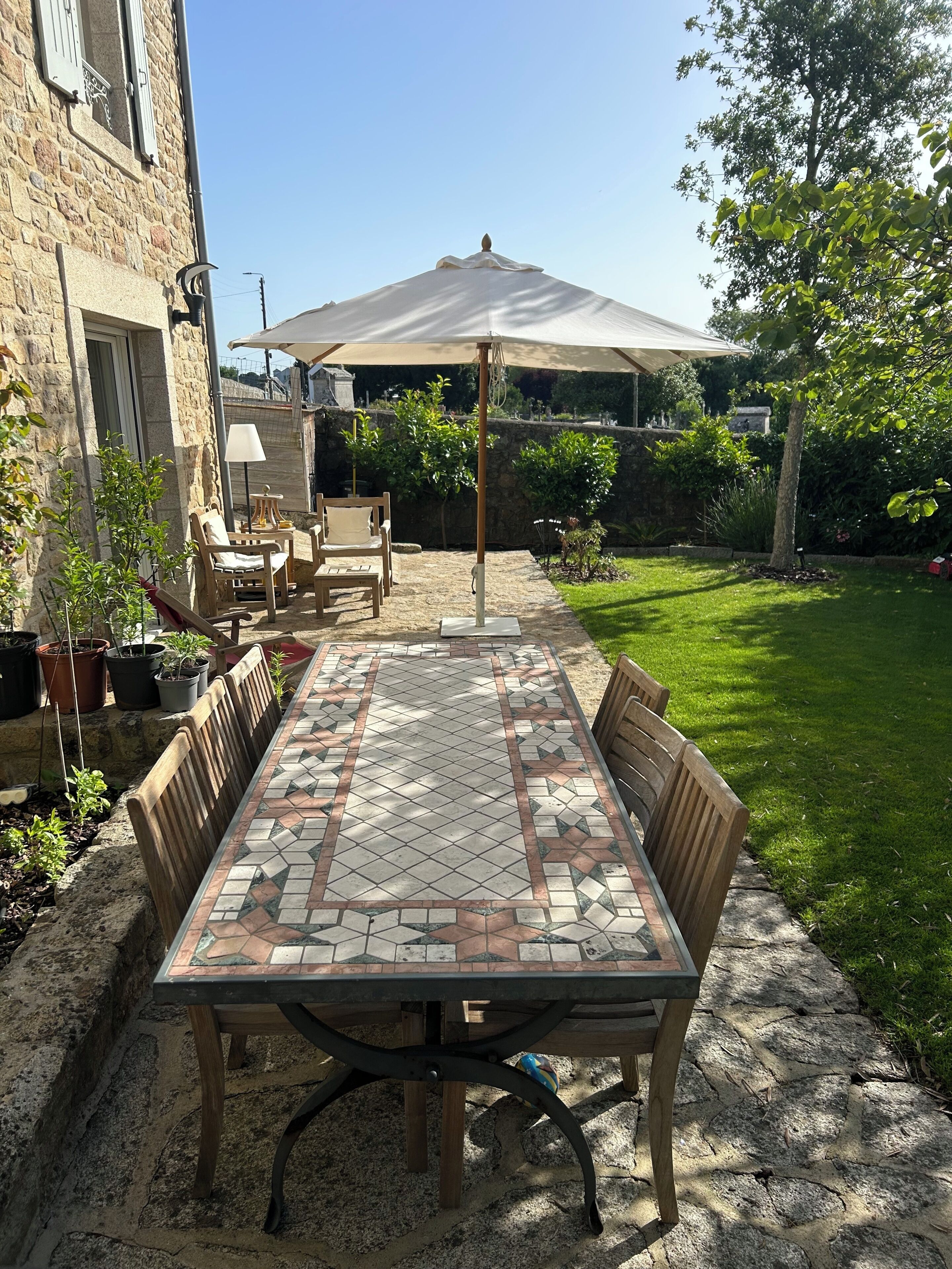 A patio with a tiled table, chairs, and an umbrella.