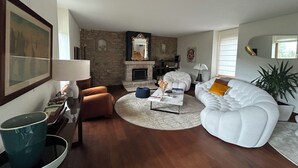 Ein Wohnzimmer mit Kamin aus Stein, einem weißen Sofa, einem Couchtisch und einem großen Gemälde an der Wand.