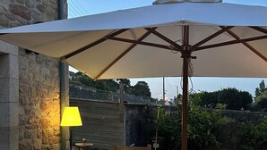 Ein Sitzbereich im Freien mit Steinmauern, einem Holztisch, zwei Stühlen und einem großen Sonnenschirm.