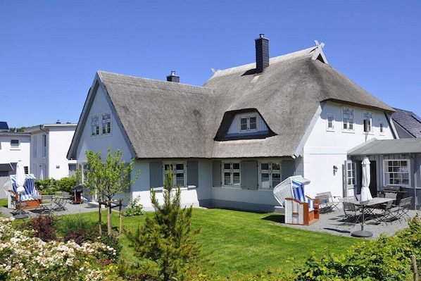 Ein Haus mit einem Reetdach, weißen Wänden und einem gepflegten Rasen.