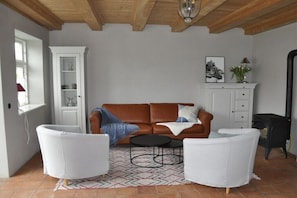 Ein Wohnzimmer mit braunem Sofa, weißen Sesseln, einem gemusterten Teppich, einem Schrank und einem Kamin.