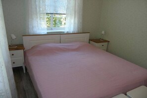 Ein Schlafzimmer mit einem Einzelbett, einem Fenster mit Vorhängen, einem Nachttisch mit Lampe und einem zusätzlichen Tisch mit Lampe.