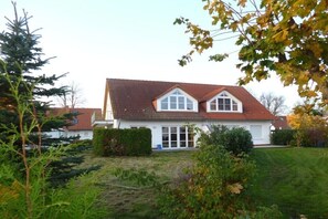 Ein zweistöckiges Haus mit rotem Ziegeldach, weißen Außenwänden und einem Vorgarten mit Rasen und Sträuchern.