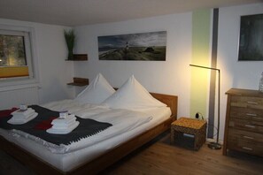 A neatly made bed with pillows and a blanket, a small bedside table, a lamp, a picture on the wall, and a wooden dresser. - Holiday home Hubertushöhe (Crinitzberg)