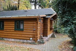 A log cabin with a stone foundation, a wooden porch, and a brick pathway leading to the entrance. - Holiday home Hubertushöhe (Crinitzberg)
