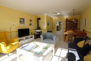 Ein Wohnzimmer mit gelbem Sofa, blauem Sessel, Couchtisch, Fernseher und Kamin.