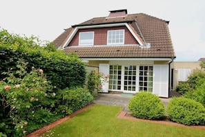Ein zweistöckiges Haus mit einem braunen Ziegeldach, einer Veranda und einem gepflegten Garten.