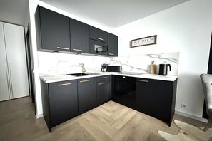 Eine moderne Küche mit schwarzen Schränken, einer Marmor-Spritzschutzwand und einem Fischgrätenboden.