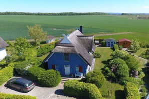A blue house with a thatched roof surrounded by greenery and a field. - Holiday home with 2 bedrooms (Putgarten)