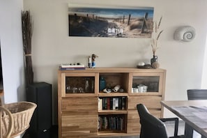 A room with a wooden bookshelf, a painting of a beach, and a shell decoration. - Holiday home with 2 bedrooms (Putgarten)