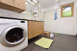A modern kitchen with a built-in washing machine, wooden cabinets, a small stool, and a green mat on the floor. - Holiday apartment in Egg with swimming pool (Egg)
