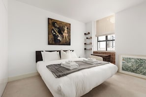 A modern hotel room with a large bed, a brick accent wall, a large window, and artwork on the walls. - New! Stunning 2BR Flat | 8 mins to Hackney Central (Greater London)
