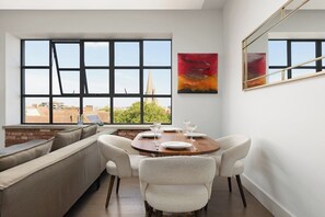 A dining area with a round table set for four, a sofa, and a large window with a city view. - New! Stunning 2BR Flat | 8 mins to Hackney Central (Greater London)