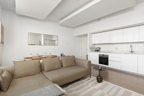 Ein modernes Wohnzimmer mit einer Couch, einem kleinen runden Tisch und einer Küchenzeile mit weißen Schränken und einer gefliesten Spritzschutzwand.