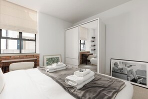 Ein modernes Hotelzimmer mit einem Bett, einem Schreibtisch, einem Sessel, einem großen Fenster und einem Spiegel.